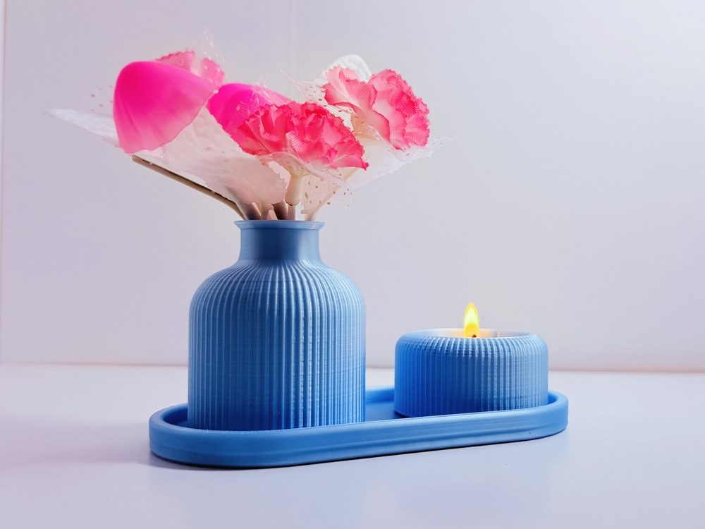 Ribbed vase with fabric flowers beside the matching tealight holder with a lit candle